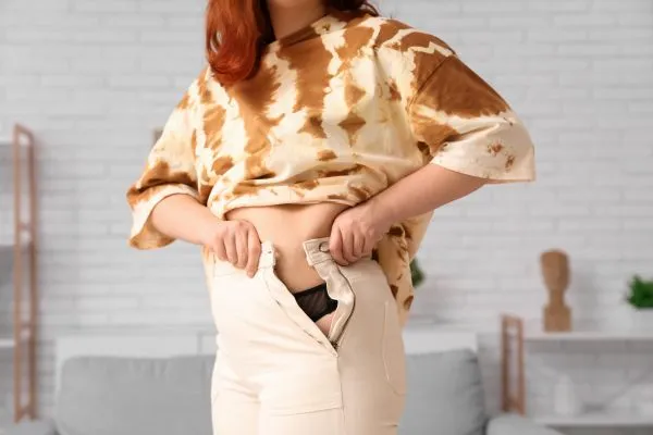 Image of woman trying to do her trousers up after pregnancy weight gain Salford Priors