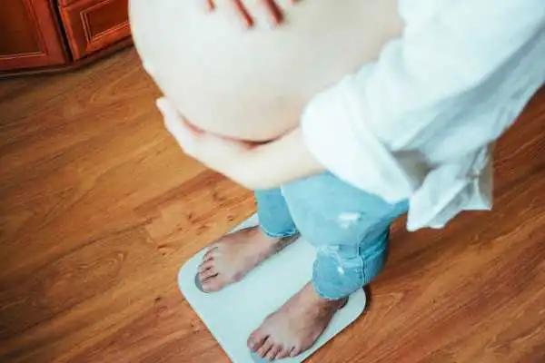 Image of woman weighing herself and experiencing weight gain through pregnancy Salford Priors